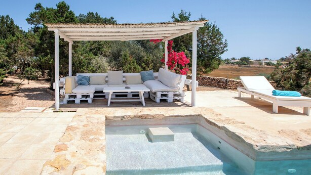 Un espace aménagé au bord de la piscine, avec une terrasse en bois, un canapé d’extérieur blanc doté de coussins et une pergola au-dessus.