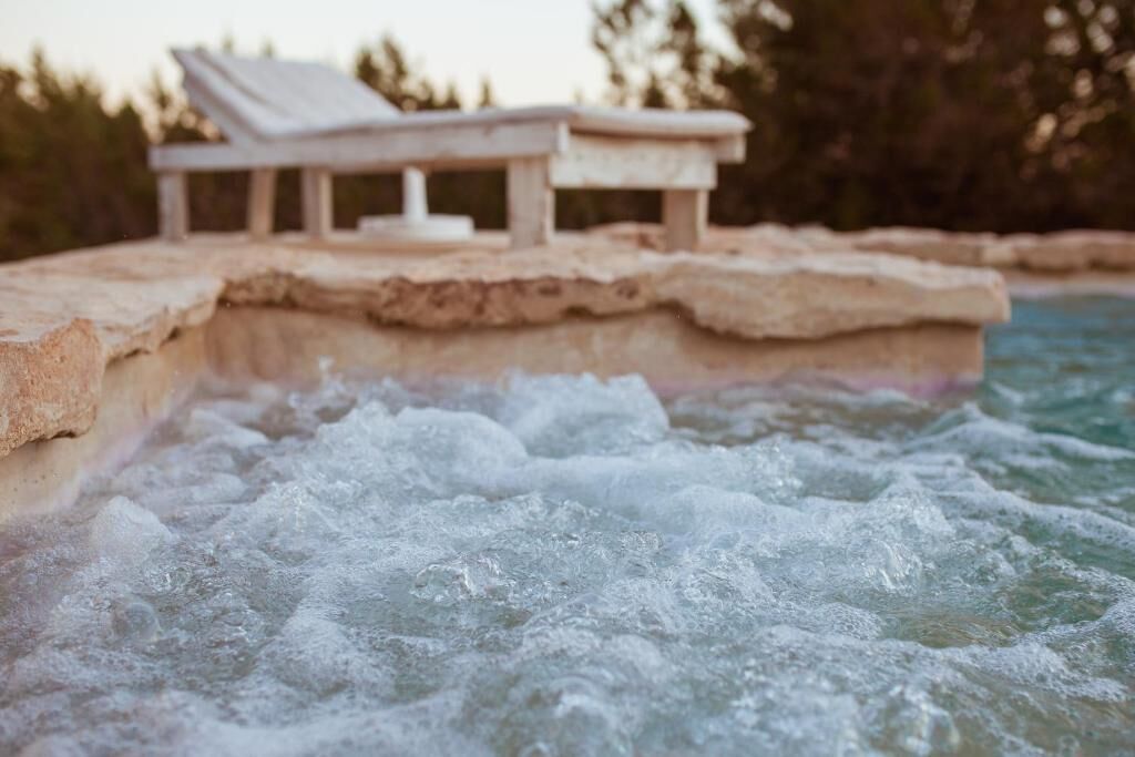Un banc de pedra amb vista a una piscina amb jocs d'aigua.