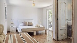 Une chambre à coucher comprenant un lit, des tables de chevet, une commode, un tapis et une porte donnant sur l’extérieur.