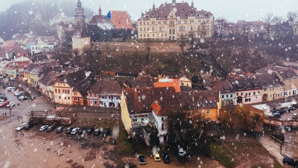 A historic town with a prominent castle-like building, surrounded by colorful buildings and a parking area. - MOLDO HOUSE, "CASA MOLDO", AT THE FOOT OF THE MEDIEVAL FORTRESS, CENTRAL (Sighișoara)