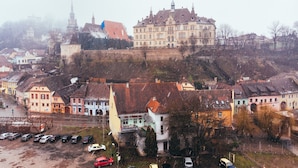 A historic building with a prominent tower, surrounded by residential buildings and a parking area. - MOLDO HOUSE, "CASA MOLDO", AT THE FOOT OF THE MEDIEVAL FORTRESS, CENTRAL (Sighișoara)