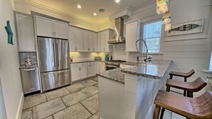 A modern kitchen with white cabinets, stainless steel appliances, a granite countertop, and wooden bar stools. - Hangtime Inlet Beach/Next to Rosemary Beach (Inlet Beach)