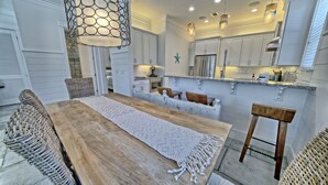 A modern kitchen with white cabinets, a wooden dining table, and a hanging light fixture. - Hangtime Inlet Beach/Next to Rosemary Beach (Inlet Beach)
