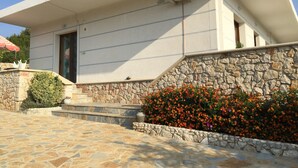 A building with a stone facade, a set of stairs leading to the entrance, and a flower bed with orange flowers. - Prefect place to spend your holidays ! (Ksamil)