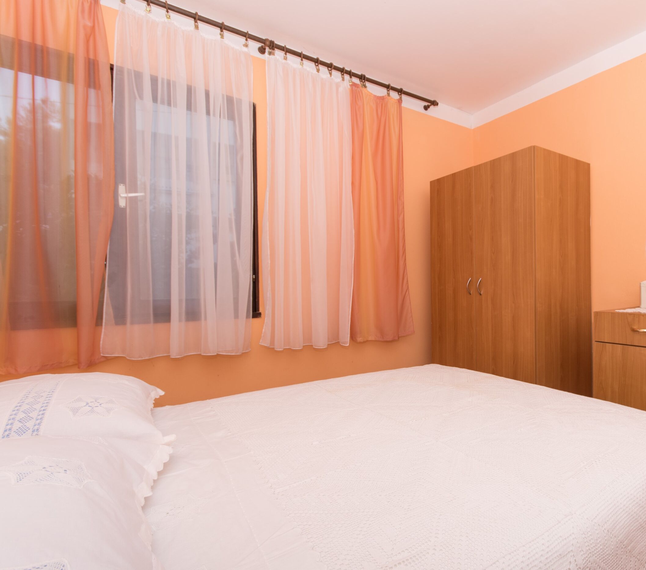 Ein Schlafzimmer mit einem Bett, einem Kleiderschrank und transparenten Vorhängen.