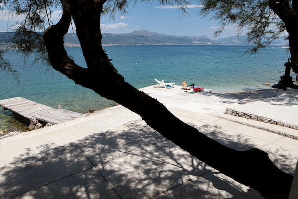A clear view of a lake with a wooden dock leading to a beach area with lounge chairs and a small statue.