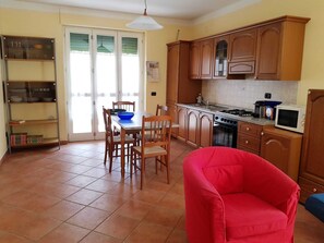 Una cocina con armarios de madera, una mesa de comedor con sillas, un sillón rojo y un microondas.