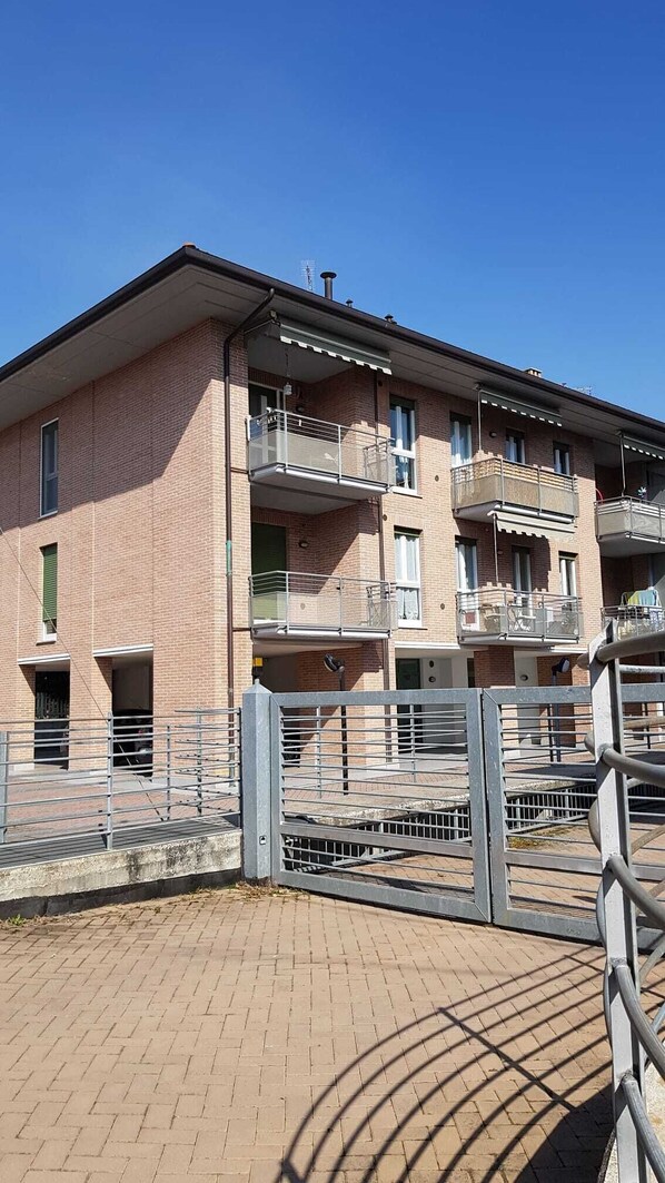 Un edificio de apartamentos de varios pisos con balcones, entrada protegida y fachada de ladrillo.