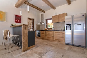 A modern kitchen with wooden cabinets, a stainless steel refrigerator, and a stone tile floor.