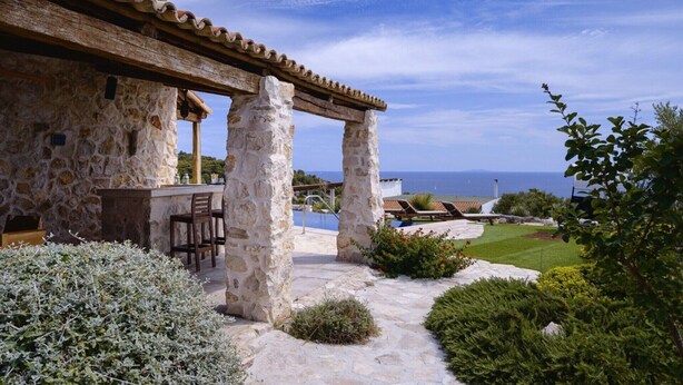 Un edificio in pietra con una pergola, posti a sedere all'aperto e vista sul mare.