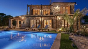 Una casa in pietra a due piani con piscina, area salotto esterna e un patio ben illuminato.