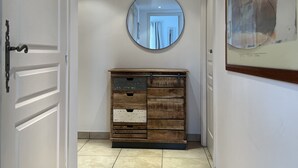 Un couloir avec une commode en bois, un miroir rond et un tableau encadré accroché au mur.