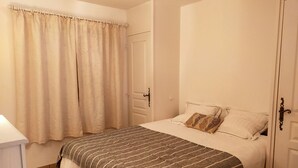 Une chambre à coucher avec un lit, des rideaux, une porte et une table de chevet.