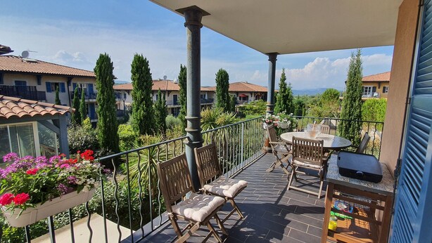 Un balcon avec une table et des chaises, un jardinière et un barbecue.