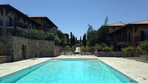 Une piscine rectangulaire à l’eau d’un bleu limpide, entourée de murs en pierre et bordée d’un chemin également en pierre.
