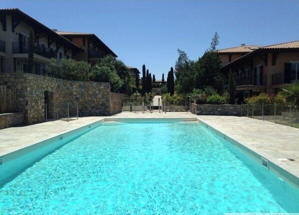A rectangular swimming pool with clear blue water, surrounded by stone walls and a stone pathway.