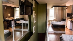 A modern hotel room with a large bed, a separate seating area, a TV, and a bathroom with a large mirror. - Cequisabe Motel (Juiz de Fora)