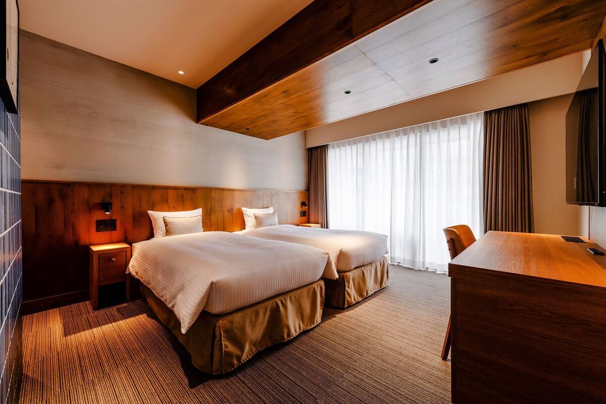 A hotel room with a large bed, a desk, a chair, a TV, and a window with curtains.
