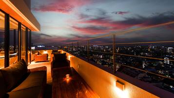 A rooftop terrace with a city view, furnished seating, and ambient lighting.