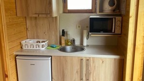 A compact kitchen with wooden cabinets, a small refrigerator, a microwave, and a window above the sink. - Chata pri Jazere 1 - Lake Side Cottage (Horná Potôn)