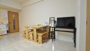 Una habitación con una mesa de madera y bancos, un mueble negro para televisión y una puerta con un espejo.