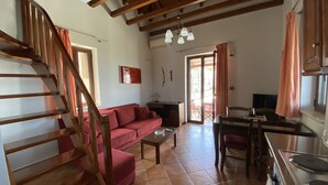Amplia sala de estar con escalera de madera, un sofá rojo, una mesa de comedor y una cocina con estufa.