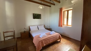 Un dormitorio con cama, cabecero de madera, mesitas de noche, una silla, ventana con cortinas y ventilador de techo.