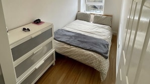 A small, well-lit bedroom with a bed, a dresser, a window, and a hanging light fixture. - 1-bed Apartment Next to Paisley Gilmour Station! (Paisley)