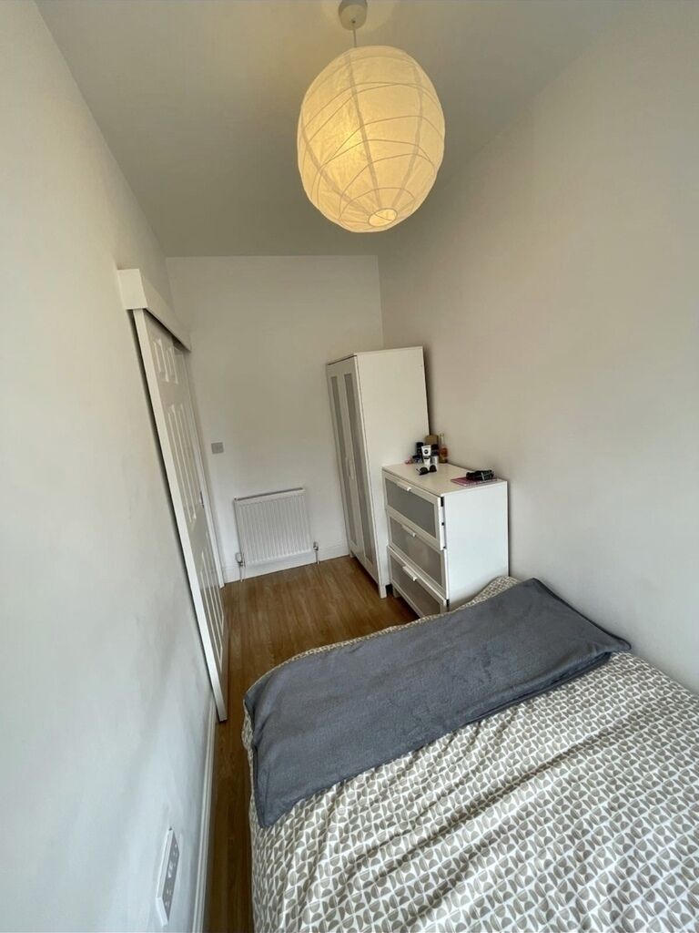 A narrow, well-lit room with a bed, dresser, and radiator.