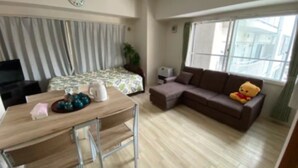 A room with a wooden dining table, chairs, a sofa, a teddy bear, a TV, and a window with curtains. - IKminami6jo residence 601 (Sapporo)