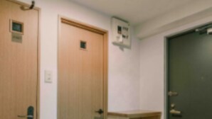 A room with two wooden doors, a small shelf with shoes, and a dark door with a white object on it. - IKminami6jo residence 601 (Sapporo)