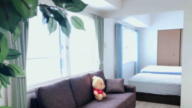 A room with a brown sofa, a bed with a blue and white striped bedspread, and a large window with curtains. - IKminami6jo residence 601 (Sapporo)
