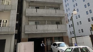 A multi-story building with a central entrance, a security guard, and a white car parked in front. - IKminami6jo residence 601 (Sapporo)