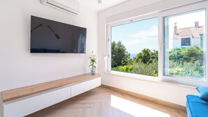 Un soggiorno moderno con un'ampia finestra, una TV a parete e una panca in legno.