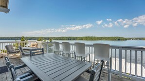 Ein Deck mit Tisch und Stühlen mit Blick auf einen See, ein Holzgeländer und eine Ansicht der bewaldeten Uferlinie.