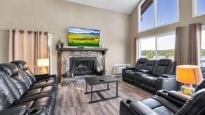 Ein Wohnzimmer mit Ledersofas, einem Kamin, einem Fernseher und Seeblick.