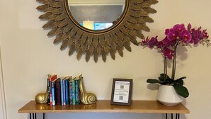Une console en bois agrémentée d’un miroir décoratif, de livres, d’un panneau encadré et d’une orchidée en pot.