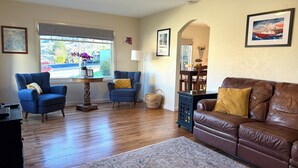Un salon avec un canapé en cuir marron, deux fauteuils bleus, une table basse en bois et un tapis à motifs.