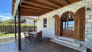A covered patio with a stone wall, wooden shutters, and a table with chairs. - Executive Villa Scorpidi With Private Pool (Lefkada)