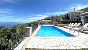 A pool area with stone flooring, a clear blue pool, and a view of the surrounding landscape. - Executive Villa Scorpidi With Private Pool (Lefkada)