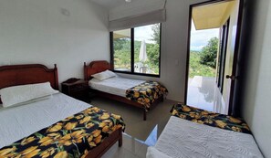 Two single beds with floral-patterned bedspreads, a nightstand, and a window offering a view of lush greenery.