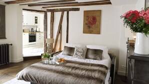 A bedroom with a bed, a bedside table, a nightstand, a window, and a view of a kitchen. - Ecrin Robespierre - Cosy & Romantic apartment with A/C in historical property (Paris)