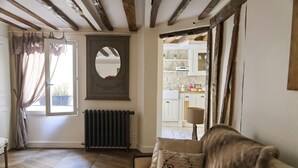 A cozy living room with a wooden floor, a sofa with a 'Paris' pillow, a radiator, and a view into the kitchen. - Ecrin Robespierre - Cosy & Romantic apartment with A/C in historical property (Paris)