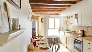 A kitchen with wooden beams, white cabinets, and a dining table set for four. - Ecrin Robespierre - Cosy & Romantic apartment with A/C in historical property (Paris)