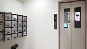 A hallway with a row of beige lockers on the left and a door with a digital elevator display on the right. - Shimaya Building 505 (Sapporo)