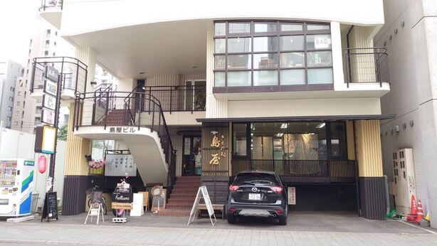A modern building with a large entrance, a staircase leading to an upper level, and a car parked in front. - Shimaya Building 505 (Sapporo)