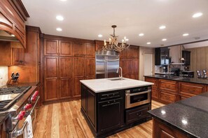 Una cocina con armarios de madera, un refrigerador de acero inoxidable, un horno empotrado e una isla central con pileta.