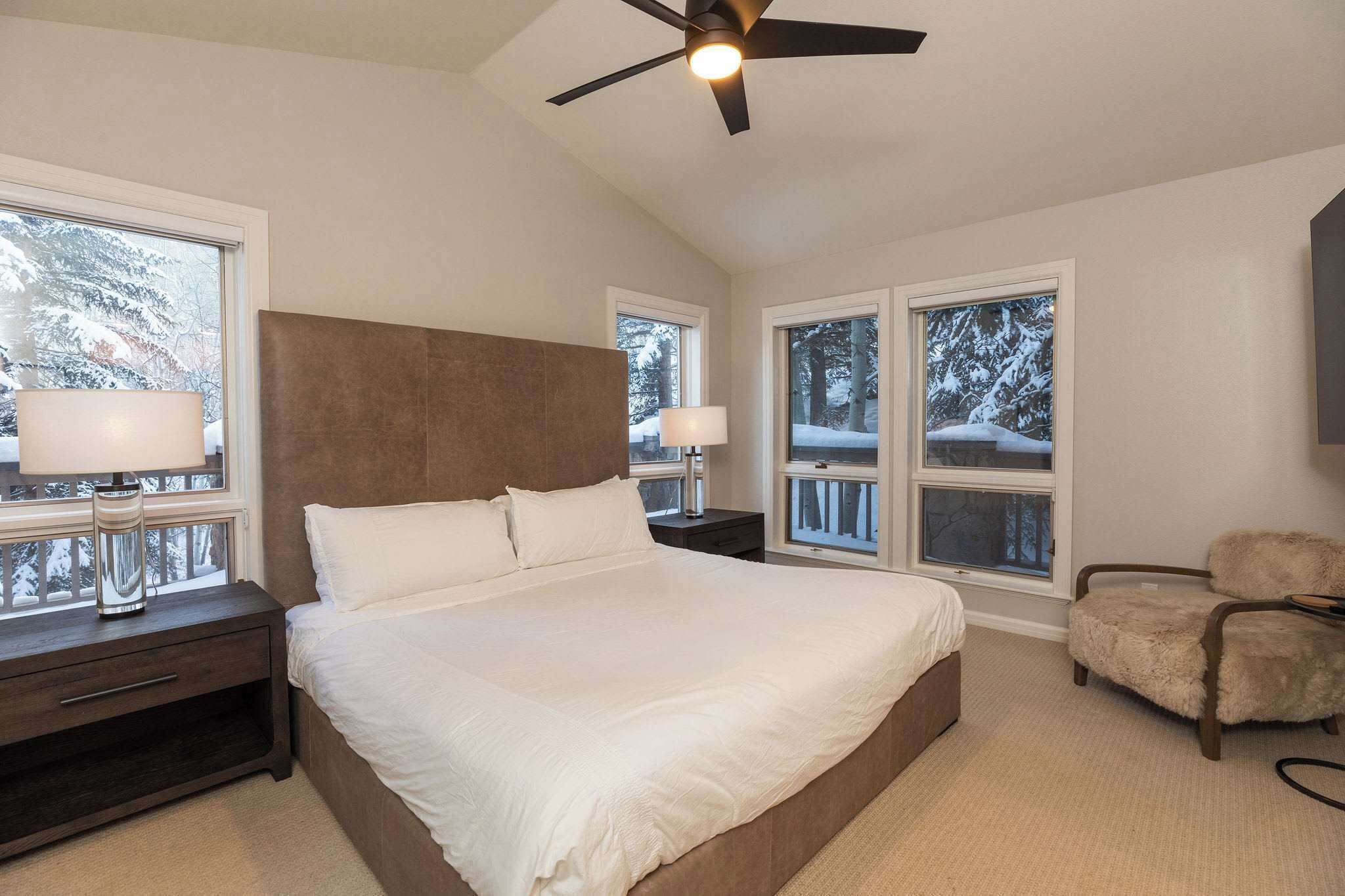 Une chambre avec un grand lit, un ventilateur de plafond et des fenêtres donnant sur des arbres couverts de neige.