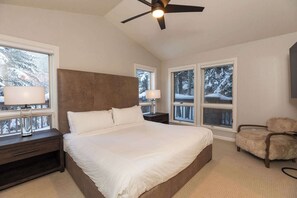 Un dormitorio con una cama grande, un ventilador de techo y ventanas con vistas a árboles cubiertos de nieve.