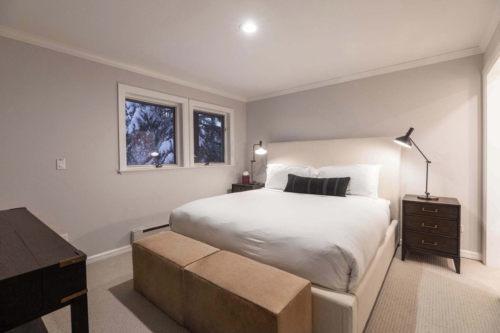 A bedroom with a bed, bedside tables, a bench, and a window with a view of trees.